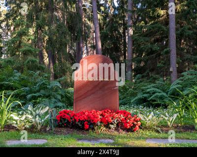 Stockholm, Suède - juin 28 2021 : Pierre de tête sur la tombe de Greta Garbo. Fleurs rouges et blanches autour de la pierre. Fond de forêt et aucune personne visible. Banque D'Images