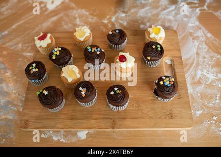 Cupcake, glaçage et saupoudres sur planche de bois pour manger, fête d'anniversaire et déjeuner dans la maison. Muffins, gâteau et chocolat ou collation à saveur vanille pour Banque D'Images