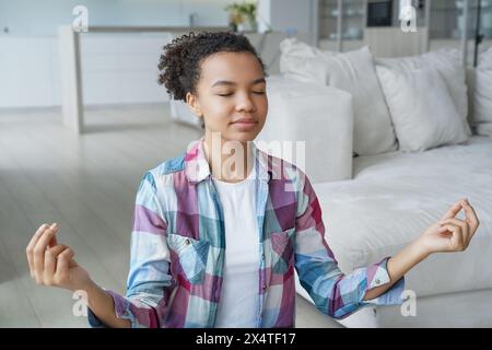 Jeune personne paisible pratiquant la méditation, trouvant l'équilibre dans un cadre de maison serein. Banque D'Images