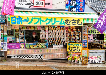 Magasin de crème glacée sous la pluie à Iwakuni, Japon. Affiche à l'extérieur de nombreux cônes en plastique de crèmes glacées de différentes saveurs, avec le propriétaire à la trappe de service Banque D'Images