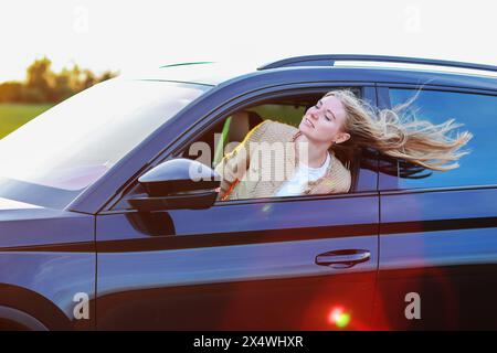 fille regarde par la fenêtre de la voiture et le vent souffle ses cheveux Banque D'Images