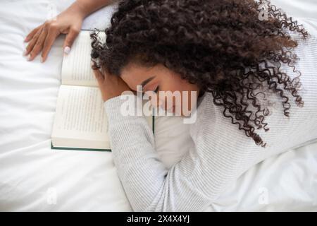 Jeune femme se reposant sur son lit après avoir lu un livre Banque D'Images