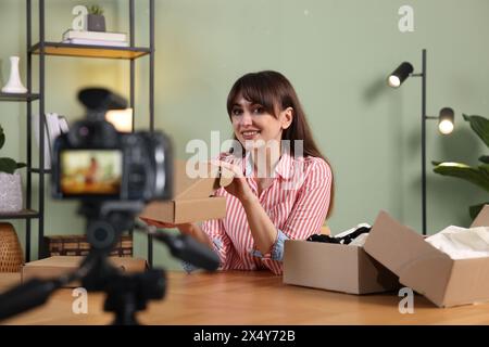Blogueur de mode souriant enregistrant une vidéo tout en déballant un colis avec des vêtements à la maison Banque D'Images