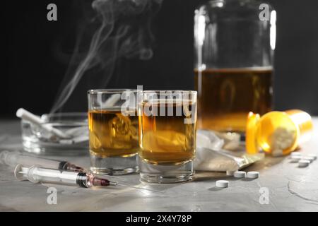 Alcoolisme et toxicomanie. Whisky dans des verres, seringues, pilules et cocaïne sur table grise Banque D'Images
