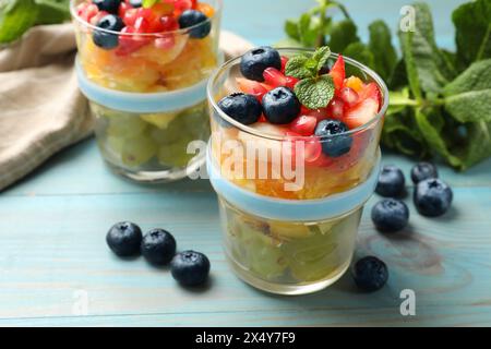 Délicieuse salade de fruits dans des verres, baies fraîches et menthe sur une table en bois bleu clair Banque D'Images