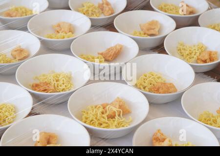 Plusieurs bols blancs contenant des nouilles jaunes, des aliments frits et des boulettes de viande sans sauce sur la table Banque D'Images