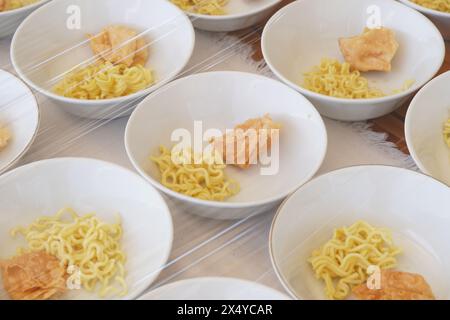 Plusieurs bols blancs contenant des nouilles jaunes, des aliments frits et des boulettes de viande sans sauce sur la table Banque D'Images