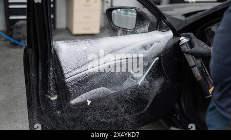 Un homme pulvérise de la mousse nettoyante sur l'intérieur d'une voiture. Banque D'Images