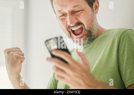 Homme heureux a reçu un message texte satisfaisant sur smartphone mobile, focus sélectif Banque D'Images