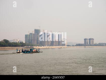 Van Pak Len, Laos - 28 mars 2024 : un cargo passe devant des bâtiments résidentiels hirise sous construction sur les rives du Mékong. Banque D'Images