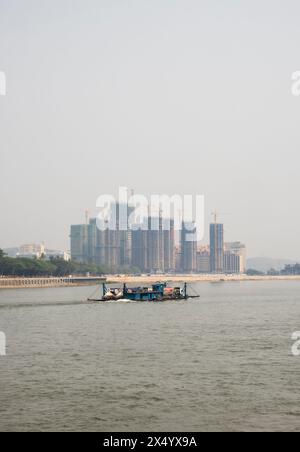 Van Pak Len, Laos - 28 mars 2024 : un cargo passe devant des bâtiments résidentiels hirise sous construction sur les rives du Mékong. Banque D'Images