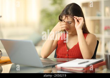 Étudiant portant des lunettes souffrant de fatigue oculaire avec un ordinateur portable à la maison Banque D'Images