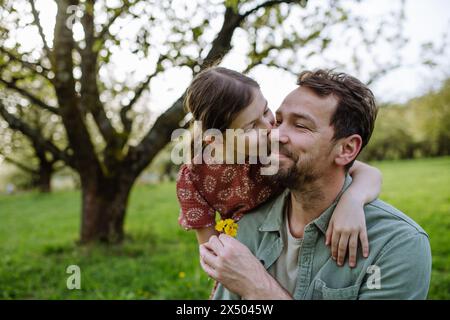 Fille donnant au père une petite fleur, l'embrassant sur la joue. Papa et fille passent ensemble du temps dans la nature printanière. Concept de fête des pères. Banque D'Images