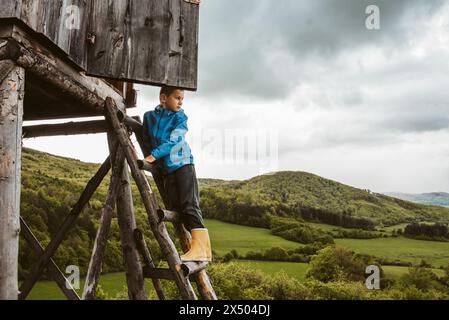 Garçon sur l'échelle de chasse aveugle pendant leur promenade dans la forêt, grimpant pour observer la belle nature printanière, la faune. Banque D'Images