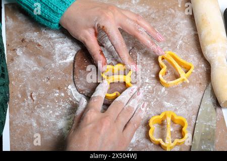 Une femme forme un pain d'épices en utilisant un moule en plastique sur une pâte roulée. La surface de travail est en farine, les outils se trouvent à côté. Cuisson du pain d'épices. Banque D'Images