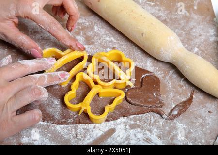 Une femme forme un pain d'épices en utilisant un moule en plastique sur une pâte roulée. La surface de travail est en farine, les outils se trouvent à côté. Cuisson du pain d'épices. Banque D'Images