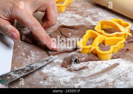 Une femme forme un pain d'épices en utilisant un moule en plastique sur une pâte roulée. La surface de travail est en farine, les outils se trouvent à côté. Cuisson du pain d'épices. Banque D'Images