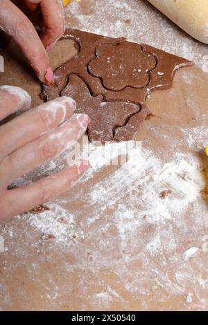 Une femme forme un pain d'épices en utilisant un moule en plastique sur une pâte roulée. La surface de travail est en farine, les outils se trouvent à côté. Cuisson du pain d'épices. Banque D'Images