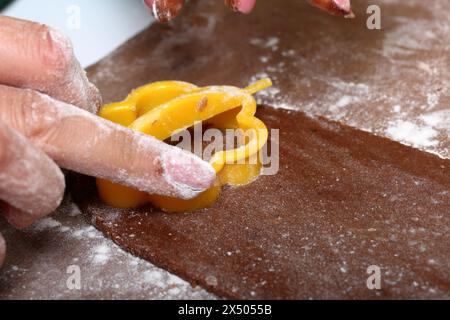 Une femme forme un pain d'épices en utilisant un moule en plastique sur une pâte roulée. La surface de travail est en farine, les outils se trouvent à côté. Cuisson du pain d'épices. Banque D'Images