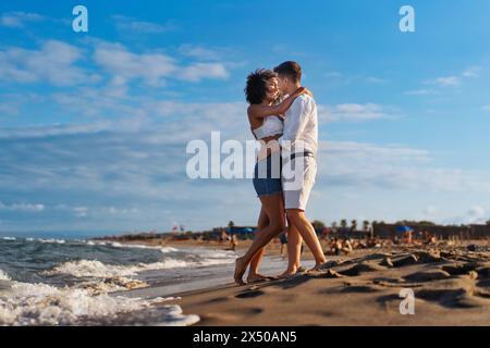 Jeune couple romantique - embrassant avec amour sur une plage de sable, profitant d'un moment joyeux au coucher du soleil au bord de la mer - affectueux, chaleureux. Banque D'Images