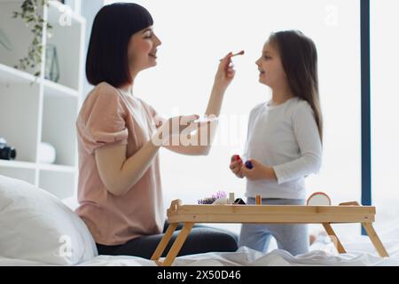 Femme heureuse applique le maquillage avec pinceau sur le visage de la petite fille. Banque D'Images