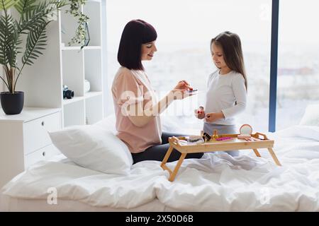 Femme heureuse applique le maquillage avec pinceau sur le visage de la petite fille. Banque D'Images