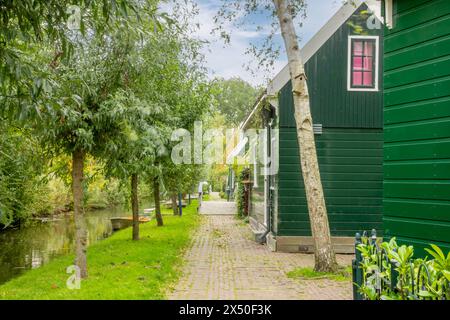 Pays-Bas. Journée d'été venteuse à Zaanse Schans. Maisons rurales typiques en bois et un bateau sur un petit canal Banque D'Images