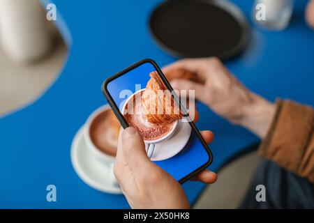 Vue aérienne d'un homme photographiant sa main trempant un croissant dans une tasse de café Banque D'Images