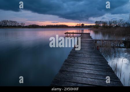 Longue jetée en bois sur le lac au coucher du soleil nuageux, vue sur un soir de printemps Banque D'Images