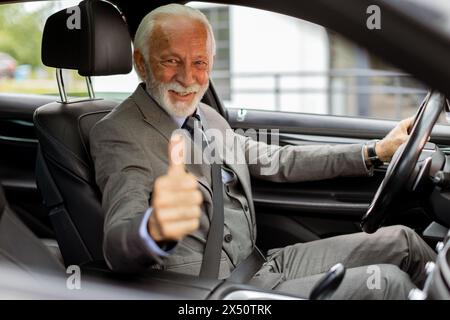 Un homme âgé en costume sourit avec l'approbation du siège du conducteur Banque D'Images