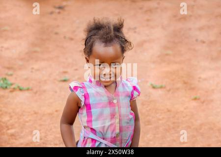 village africain, petite fille heureuse avec un cheveu sauvage jouant dans la cour de sable Banque D'Images