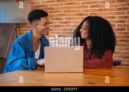 Heureux homme multiethnique et femme conversent et surfent sur Internet sur un ordinateur portable. Banque D'Images