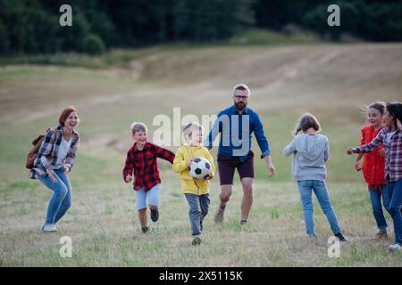 Jeunes élèves jouant avec le professeur en plein air, dans la nature, pendant la classe d'enseignement sur le terrain, courir avec le ballon. Enseignants dévoués pendant l'activité en plein air Banque D'Images