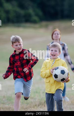 Jeunes élèves jouant avec le professeur en plein air, dans la nature, pendant la classe d'enseignement sur le terrain, courir avec le ballon. Enseignants dévoués pendant l'activité en plein air Banque D'Images