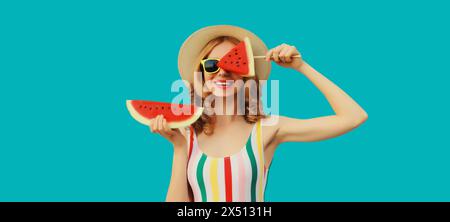 Portrait d'été de jeune femme heureuse avec des fruits juteux frais, sucette et tranche de pastèque portant un chapeau de paille, lunettes de soleil sur fond bleu Banque D'Images