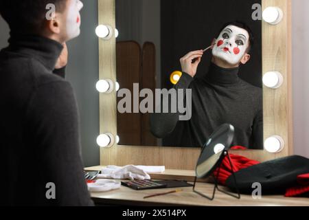 Jeune homme appliquant le maquillage mime près du miroir dans le vestiaire Banque D'Images