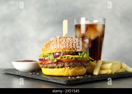 Hamburger avec délicieuse patty, boisson gazeuse, frites et sauce sur table sombre sur fond gris, gros plan Banque D'Images