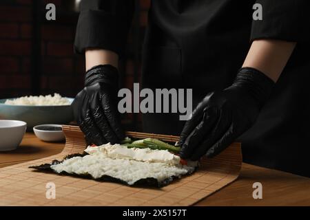 Chef en gants faisant rouler des sushis à la table en bois, gros plan Banque D'Images