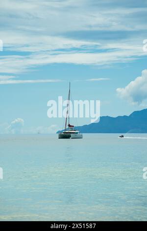 Yacht amarrage près de la belle plage de vallon, mer calme, île silhouette à l'arrière. Mahé, Seychelles Banque D'Images