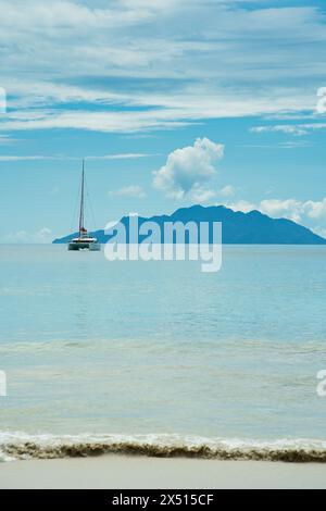 Yacht amarrage près de la belle plage de vallon, mer calme, île silhouette à l'arrière. Mahé, Seychelles Banque D'Images