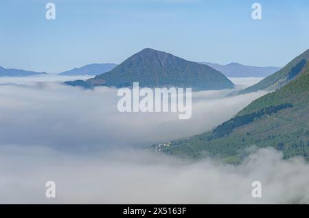 Un sommet de montagne serein s'élève au-dessus d'une couverture de brouillard tôt le matin niché dans une vallée sereine. Banque D'Images