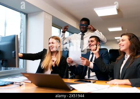 Équipe d'affaires multiethnique dans le bureau, jubilant au succès de l'écran d'ordinateur. Des collègues joyeux et diversifiés avec un ordinateur portable profitent de la victoire de l'entreprise. Excité Banque D'Images