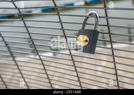 Cadenas gris simple sur une clôture en treillis métallique avec étiquette d'or avec fond hors foyer. Banque D'Images