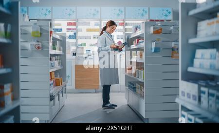 Pharmacie Drugstore : beau pharmacien chinois utilise une tablette numérique, vérifie l'inventaire de médicaments, de médicaments, de vitamines, de produits de soins de santé sur une étagère. Druggiste professionnel dans Pharma Store Banque D'Images