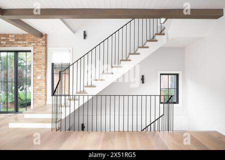 Un bel escalier avec plancher en bois et marches d'escalier, garde-corps en fer forgé, et poutres en bois à travers le plafond avec shiplap. Banque D'Images