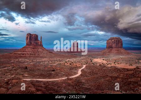 Vue spectaculaire sur la magnifique butte et les mitaines de Monument Valley pendant l'heure bleue après le coucher du soleil encadrée par des nuages colorés d'une tempête qui passe. Banque D'Images