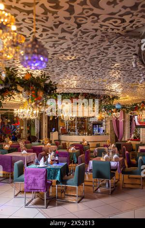Intérieur élégant du restaurant avec tables rondes, nappes violettes, lustres et décoration florale. Bouteille de vin sur la table. Banque D'Images
