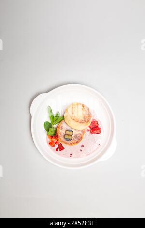 Crêpes rondes et moelleuses au fromage cottage recouvertes de fraises et de myrtilles vibrantes sur une assiette blanche, parfaites pour un délicieux petit déjeuner. Banque D'Images