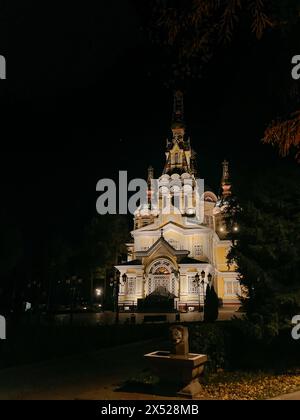 Une superbe église orthodoxe russe illuminée la nuit, avec un extérieur jaune vif, un clocher imposant, entouré d'arbres et d'un parc. Banque D'Images