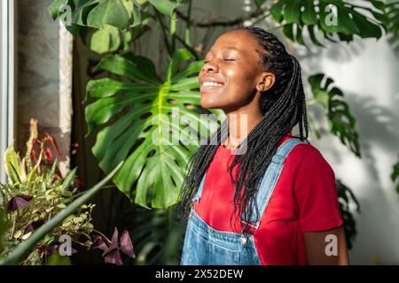 Femme noire souriante parmi le jardin intérieur. African American Happy Cheery Girl contre des feuilles de plante Banque D'Images